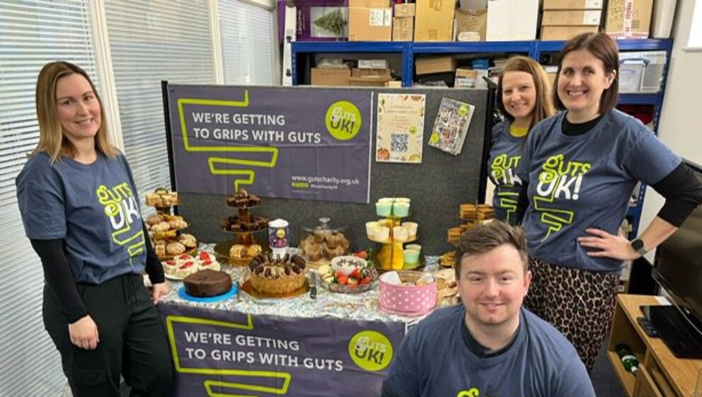 A group of colleagues from William's pumbing merchant stood next to a table full of baked goods, decorated with Guts UK branding.