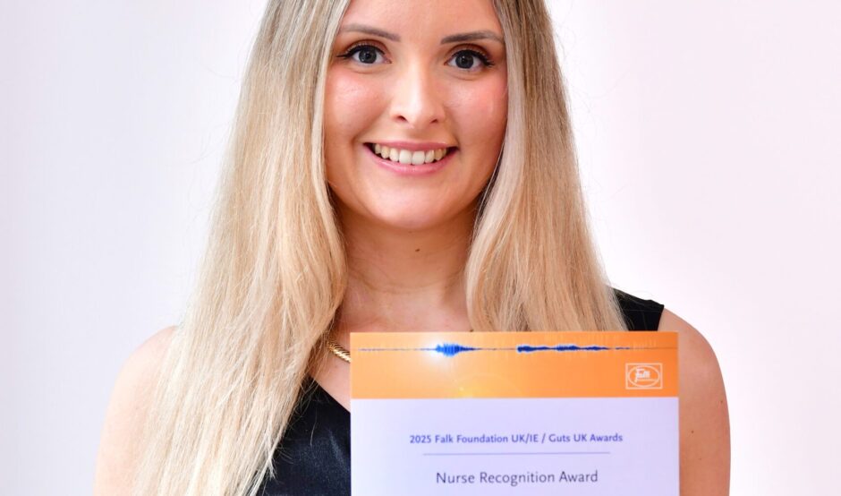 Sarah is smiling at the camera with her certificate. She has long, blonde hair and is wearing a black, sleeveless dress.