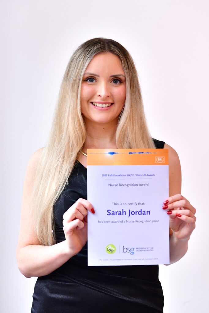 Sarah is smiling at the camera with her certificate. She has long, blonde hair and is wearing a black, sleeveless dress.