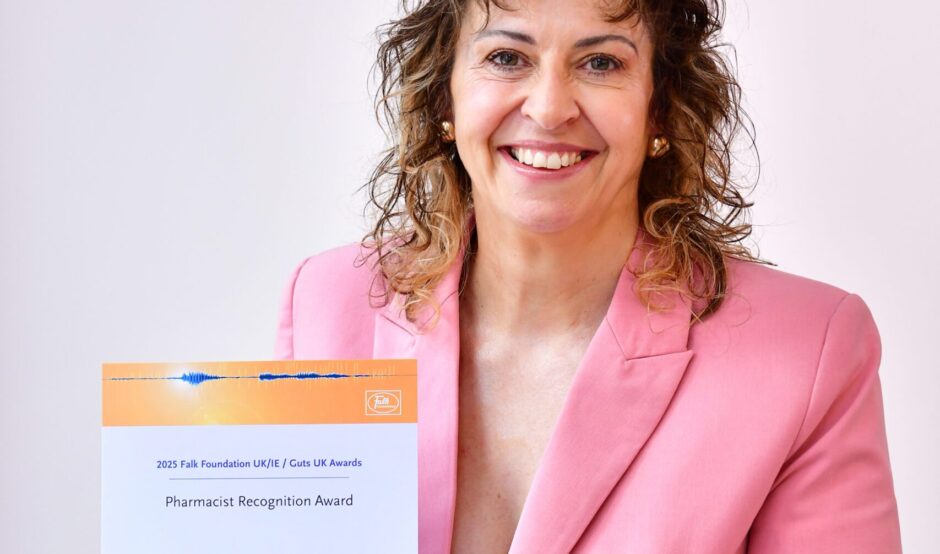 Fiona smiles at the camera, holding her certificate. She has shoulder length, curly, brown hair and wears a light pink blazer.