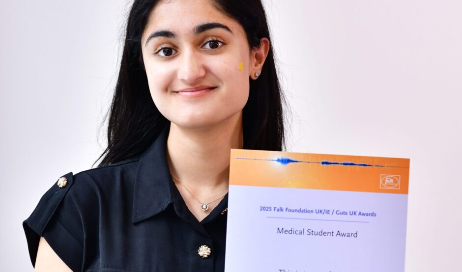 Symriti smiles at the camera with her certificate. She has black, shoulder length hair, and is wearing a dark navy, shirt style dress.