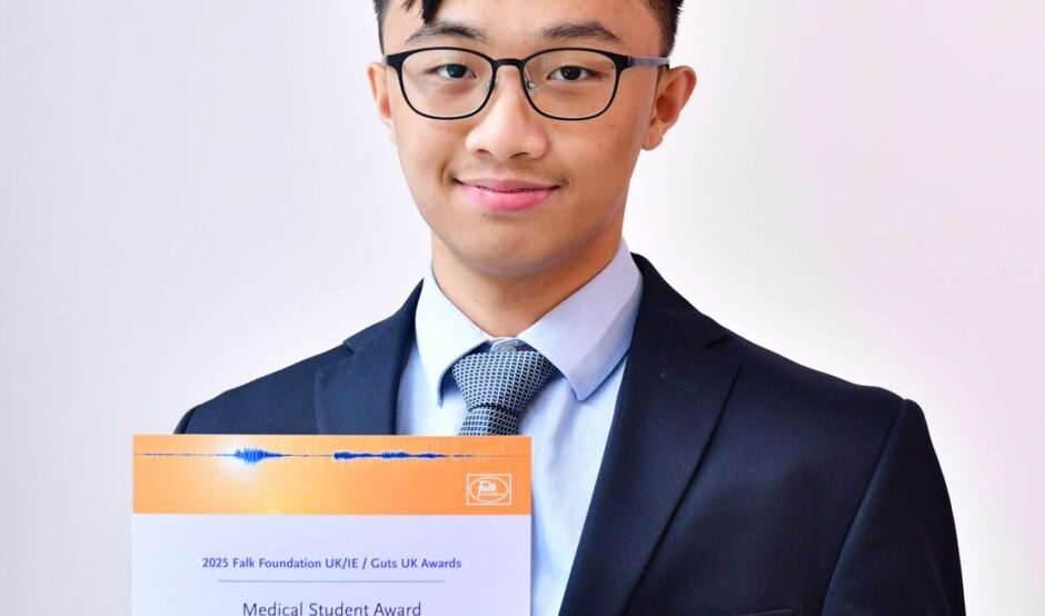 Wei Han stands with his certificate in his hands, smiling. He wears black rimmed glasses, has black hair, wears a light blue shirt, navy tie and navy suit.