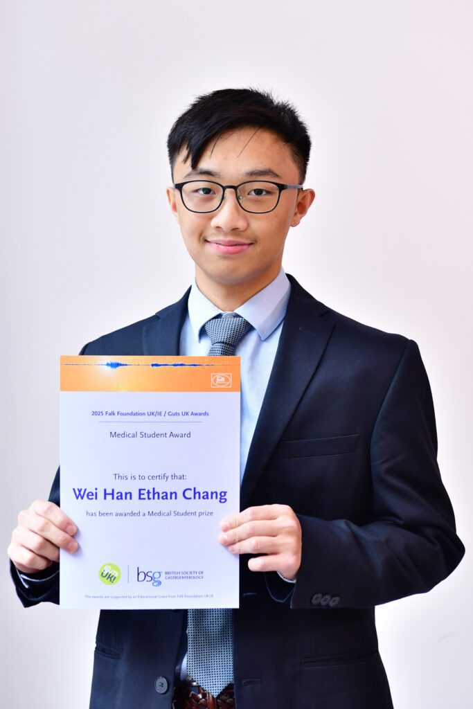 Wei Han stands with his certificate in his hands, smiling. He wears black rimmed glasses, has black hair, wears a light blue shirt, navy tie and navy suit.