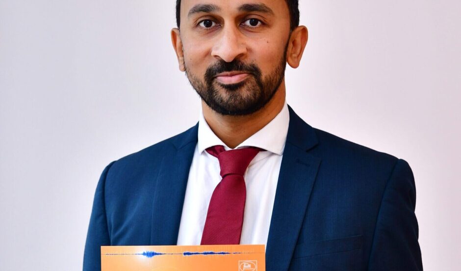 Amar smiles at the camera, holding his certificate. He has short, black hair, wears a navy suit, white shirt and deep red tie.