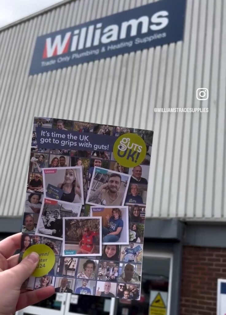 A Guts UK magazine being held up outside the front of a building that has a sign that says 'Williams'.