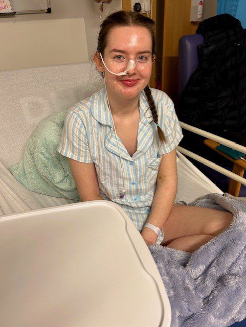 Guts UK supporter, Lucy, sat crossed legged on a hospital bed, smiling, 