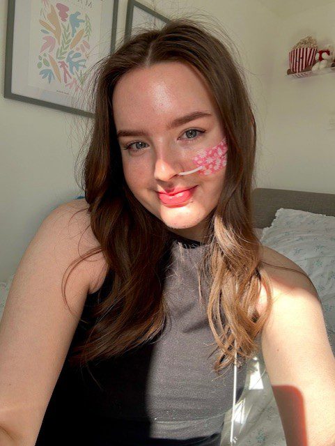 Guts UK supporter, Lucy, is sat on a bed smiling at the camera. 