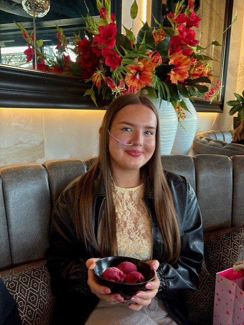 Lucy pictured sat at a restaurant table, holding a bowl of sorbet, smiling at the camera. 