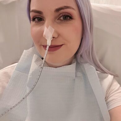 Guts UK supporter, Leanne, smiling at the camera in a selfie. Leanne has lilac coloured hair and a feeding tube inserted in her nose.