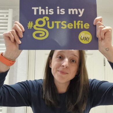 Lisa takes part in #GUTSelfie, holding up her #GUTSelfie board and showing her tummy, which is revealed by her rolled up, navy, long-sleeve top.