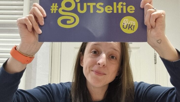 Lisa takes part in #GUTSelfie, holding up her #GUTSelfie board and showing her tummy, which is revealed by her rolled up, navy, long-sleeve top.