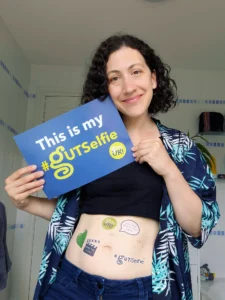 Rachael is smiling and holding a banner reading "This is my #GUTSelfie." She has several #GUTSelfie temporary tattoos on her stomach and she is smiling proudly at the camera.