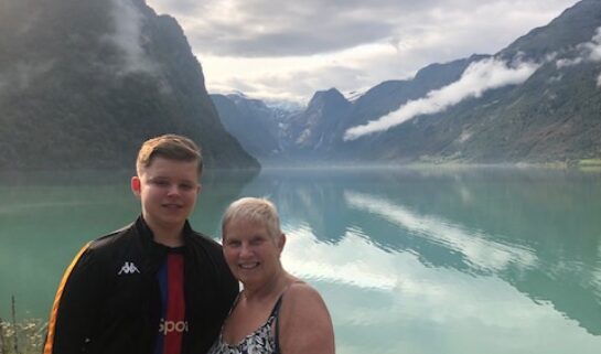 Sue (left) stands with her grandson with a backdrop of the Norwegian fjords.