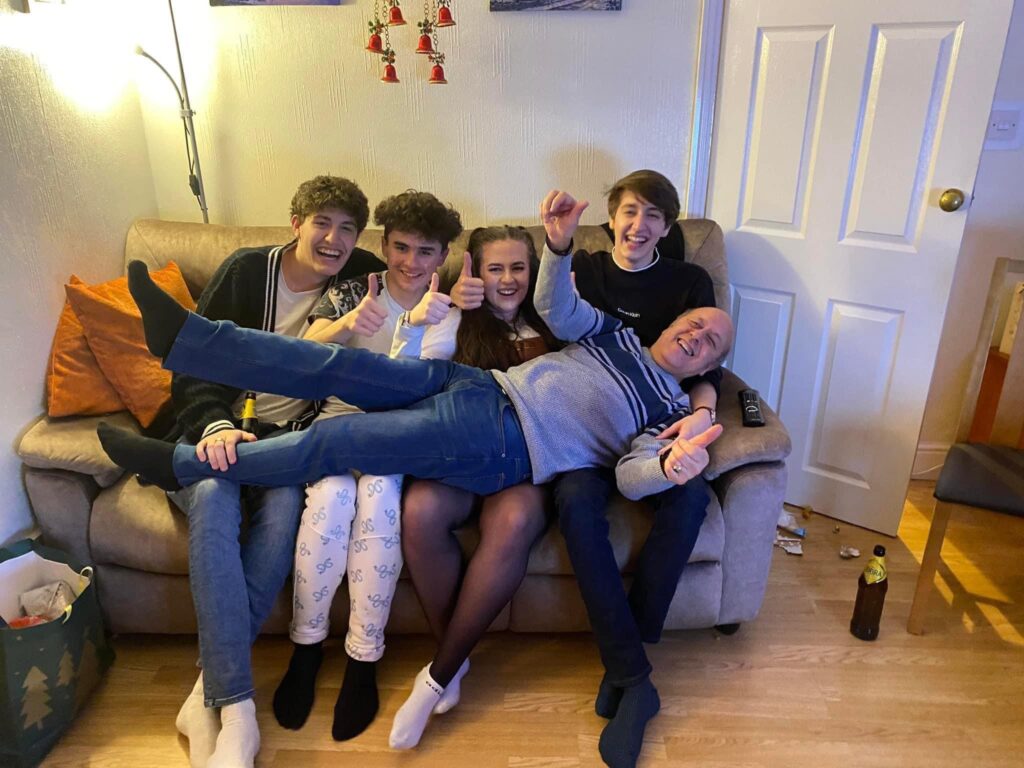 Charlie's grandchildren, sat on the sofa, with Charlie laid across their laps, grinning at the camera. 