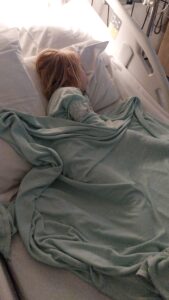 Mia sleeps peacefully under a soft, light green blanket in a hospital bed.