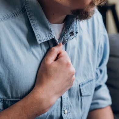 A man in a light denim blue shirt holds his hand to the centre of his chest.