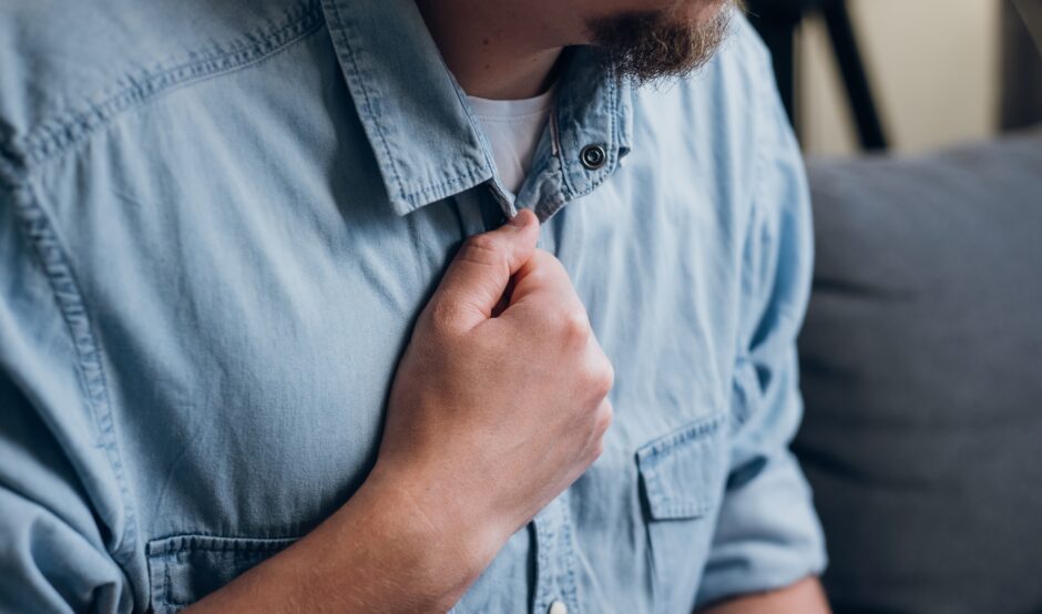 A man in a light denim blue shirt holds his hand to the centre of his chest.