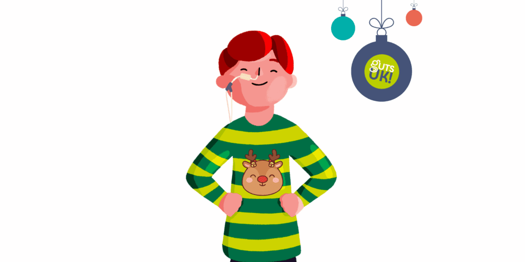 Guts UK's boy brand character is stood up with his hands on his hips, smiling. He has a feeding tube going into one nostril and three festive baubles are to the right of him.