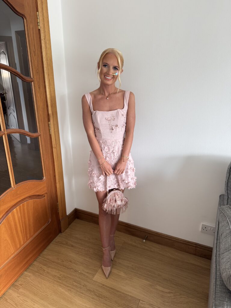 Eryn stands in a living room wearing a short, pink dress, and is holding a pink handbag.