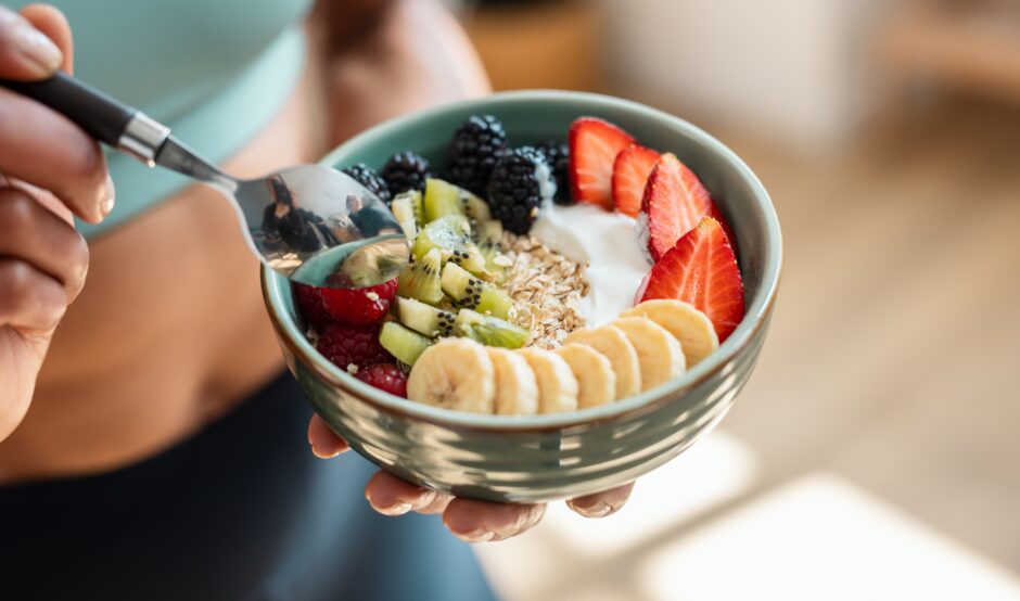 A person eating a yogurt bowel with fruit and nuts.