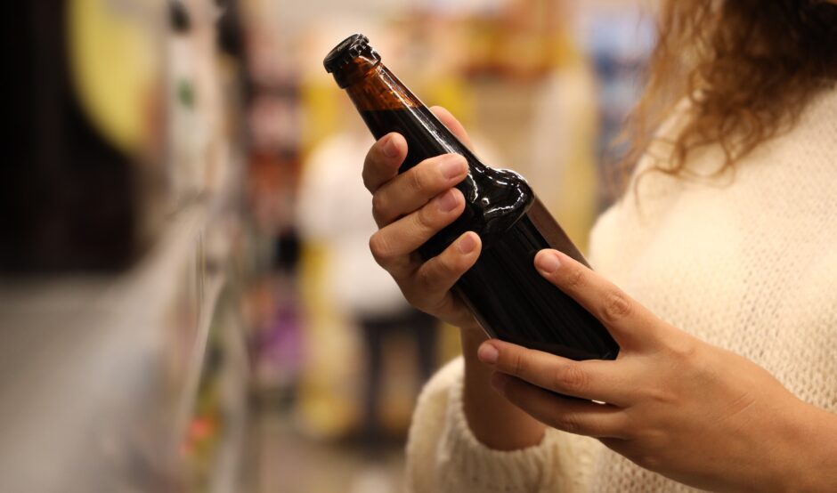 A person holds a bottle of beer in their hands in the supermarket.