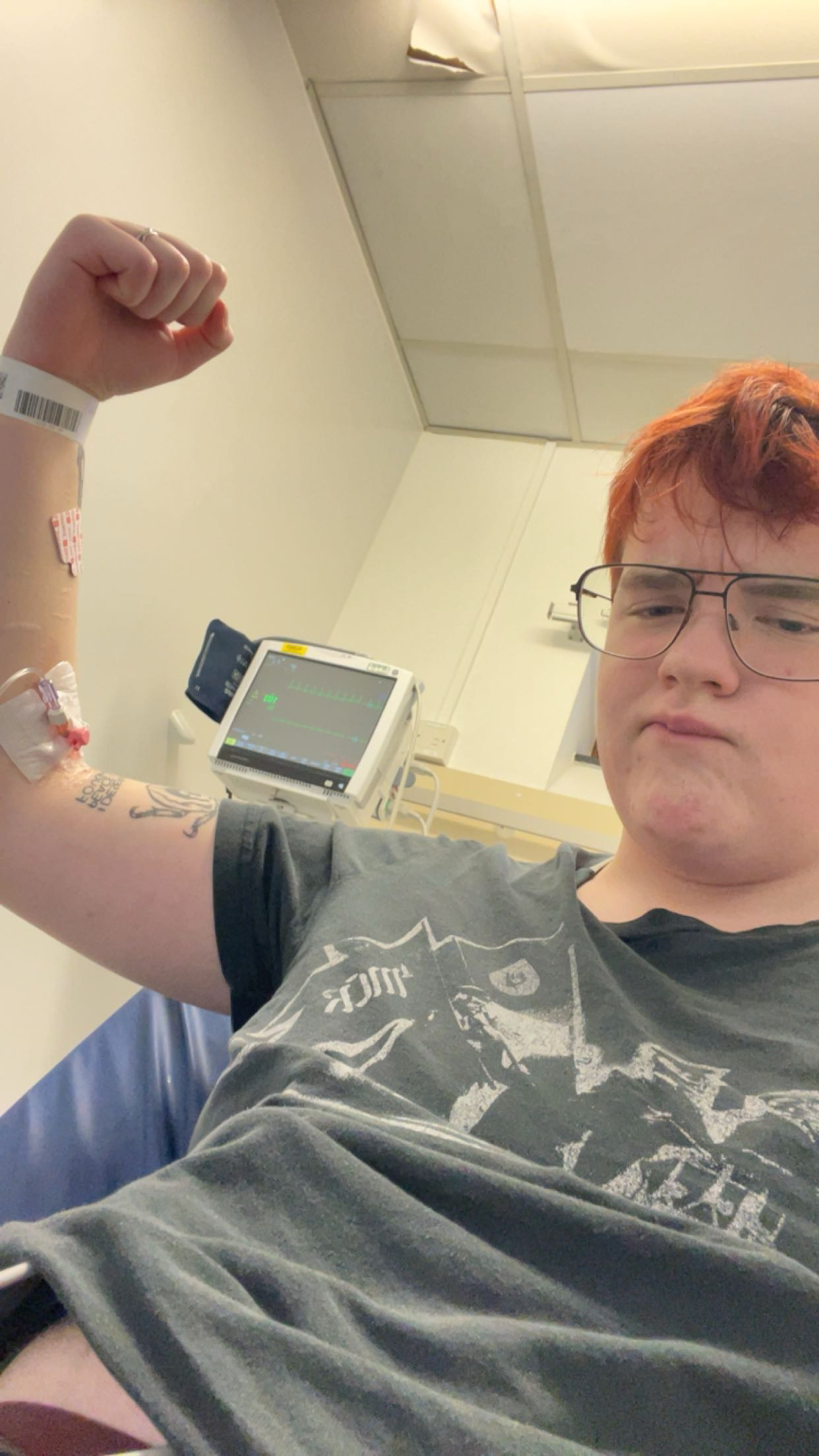 Griffin sitting in a hospital bed, flexing his arm to show a medical monitor and an IV line.