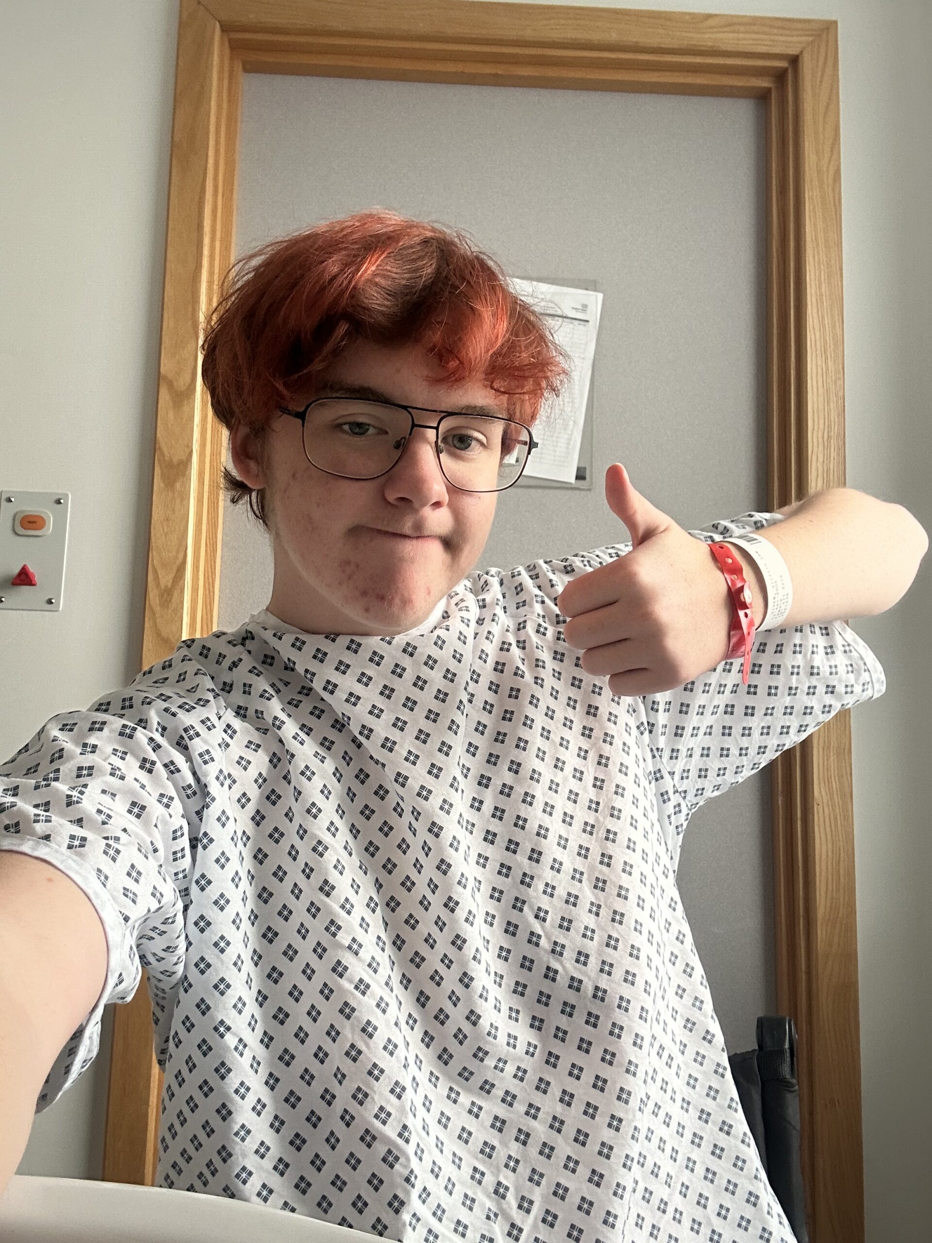 Griffin wearing a patterned hospital gown and glasses, giving a thumbs-up to the camera.