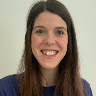 Grace has long, straight brown hair and is smiling, wearing a blue t-shirt that features the text 