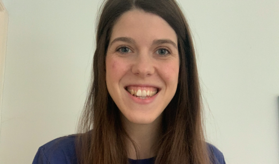 Grace has long, straight brown hair and is smiling, wearing a blue t-shirt that features the text "GUTS UK!" in white and lime green.