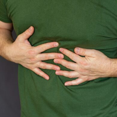 A person in a green t-shirt clutching their upper abdomen with both hands, suggesting pain or discomfort.