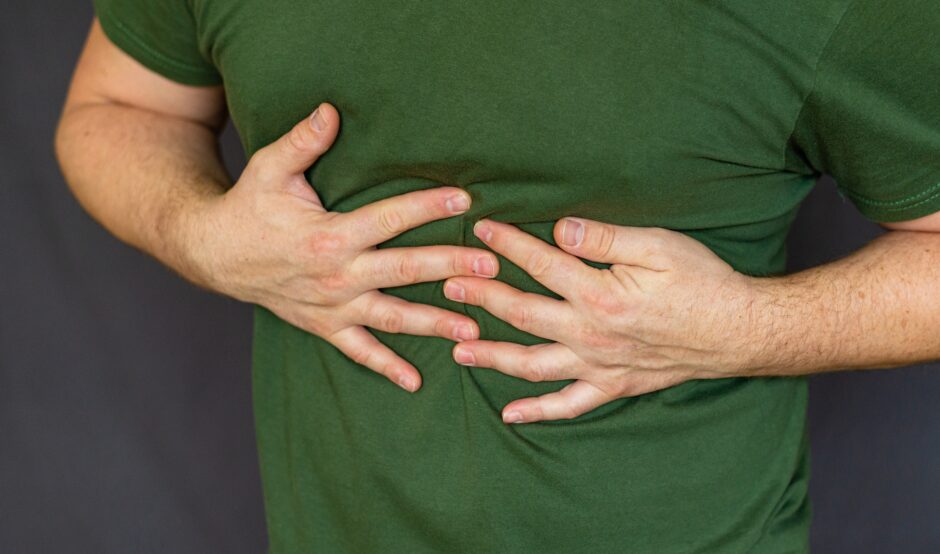 A person in a green t-shirt clutching their upper abdomen with both hands, suggesting pain or discomfort.