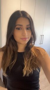 Sehba is wearing a black sleeveless top and is smiling softly at the camera. The background consists of a neutral-coloured wall and a white wardrobe with sleek vertical handles.