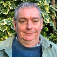 Headshot of Jon smiling, set against a background of green and yellow ivy leaves.