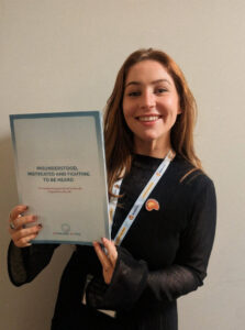 AR is smiling at the camera while proudly holding up a report titled: "Misunderstood, mistreated and fighting to be heard: The devastating journey of achalasia diagnosis in the UK" by Achalasia Action.