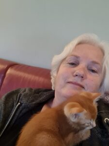 Annie, who has diverticular disease, is pictured sitting on he red sofa with her orange cat, named Leo, cuddling on her chest. 