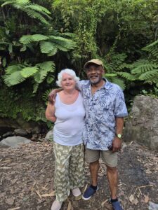 Annie is pictured on holiday in St Vincent with her husband who is hugging her. They have trees in the background and are smiling, wearing summery holiday clothes.