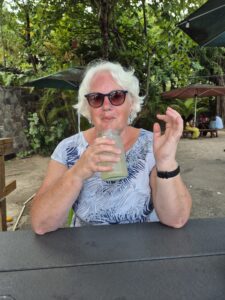 Annie is pictured on holiday in St Vincent with trees behind her sitting down, she's wearing a blue top, sunglasses and is drinking a drink 