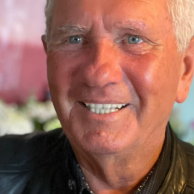 A close-up portrait of Michael smiling with short white hair, light blue eyes, and wearing a black leather jacket.