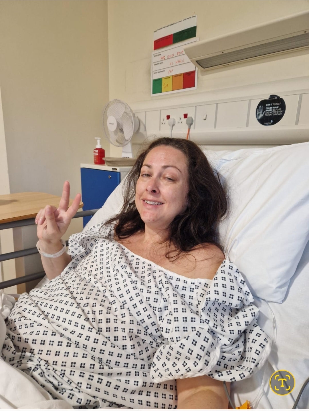 A woman with shoulder length dark hair lays in a hospital gown in a hospital bed.