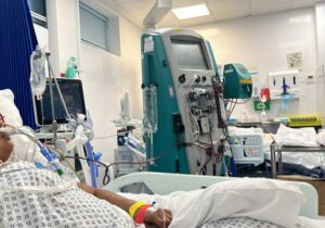 Elizabeth is lying in a hospital bed with a ventilator. 
